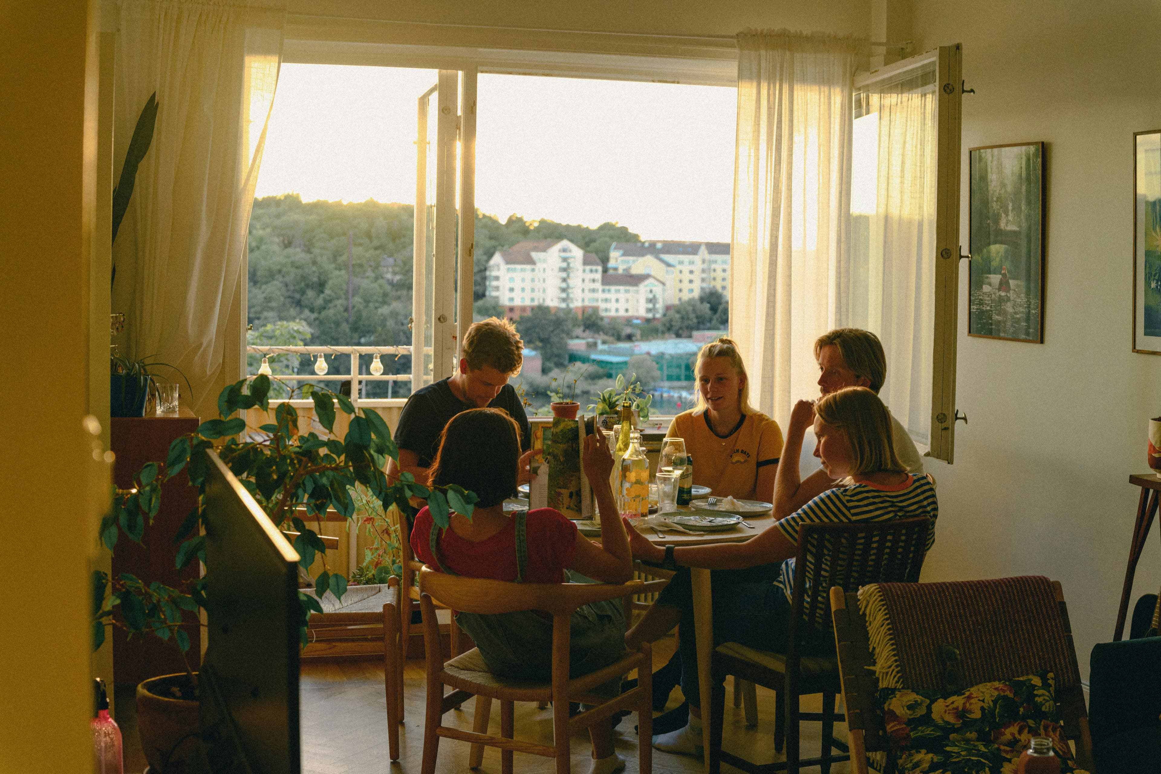 Guests sharing a meal in a sunlit apartment by an open balcony door